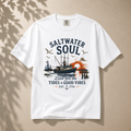A white short-sleeve crewneck t-shirt with a vintage-style nautical graphic on the front. The graphic features the text 'SALTWATER SOUL' in dark blue, a fishing boat, seagulls, a sunset in orange, and the phrase 'Lift for the Tides & Good Vibes EST.