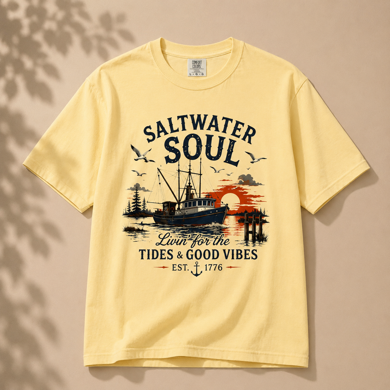 A pale yellow short-sleeve t-shirt with a vintage-style nautical graphic on the front. The graphic features the text 'SALTWATER SOUL' and 'Lawn for the TIDES & GOOD VIBES EST.