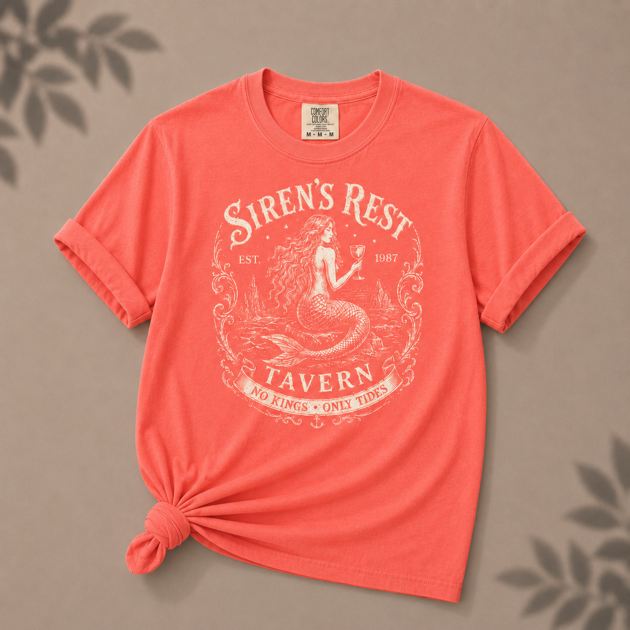 Coral t-shirt with 'Siren's Rest Tavern' graphic on a brown background