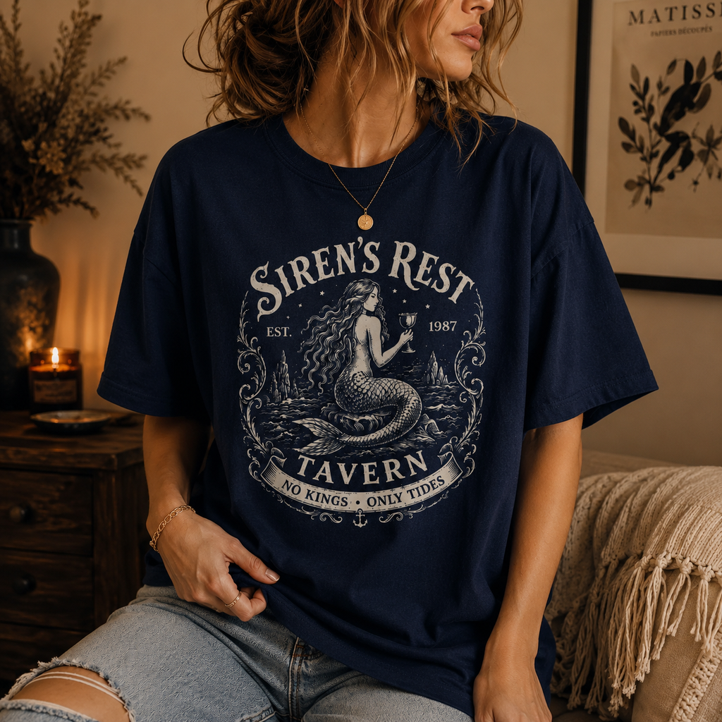 Person wearing a navy blue t-shirt with 'Siren's Rest Tavern' design in a cozy indoor setting.