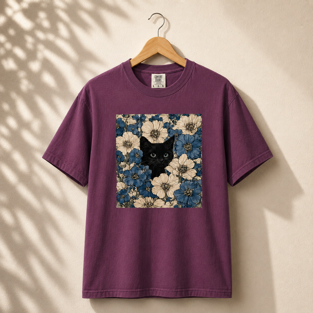 Purple t-shirt with a black cat and floral design on a wooden hanger against a beige wall.