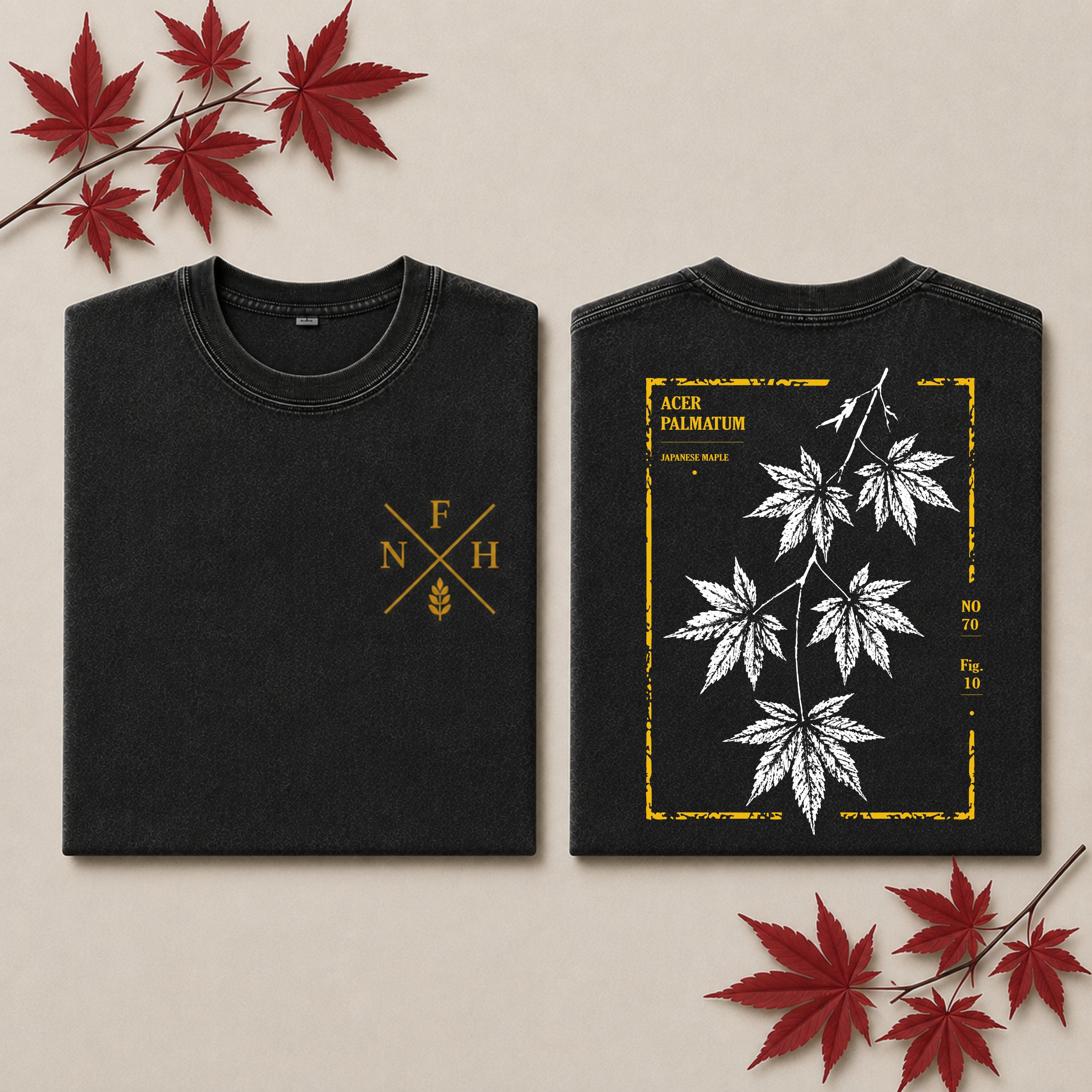 Two folded black T-shirts shown on a beige background with red maple leaves as props. The left shirt displays a gold crossed letters and wheat emblem on the chest, and the right shirt shows a back design with white maple leaves inside a distressed gold border and the text 'ACER PALMATUM'.