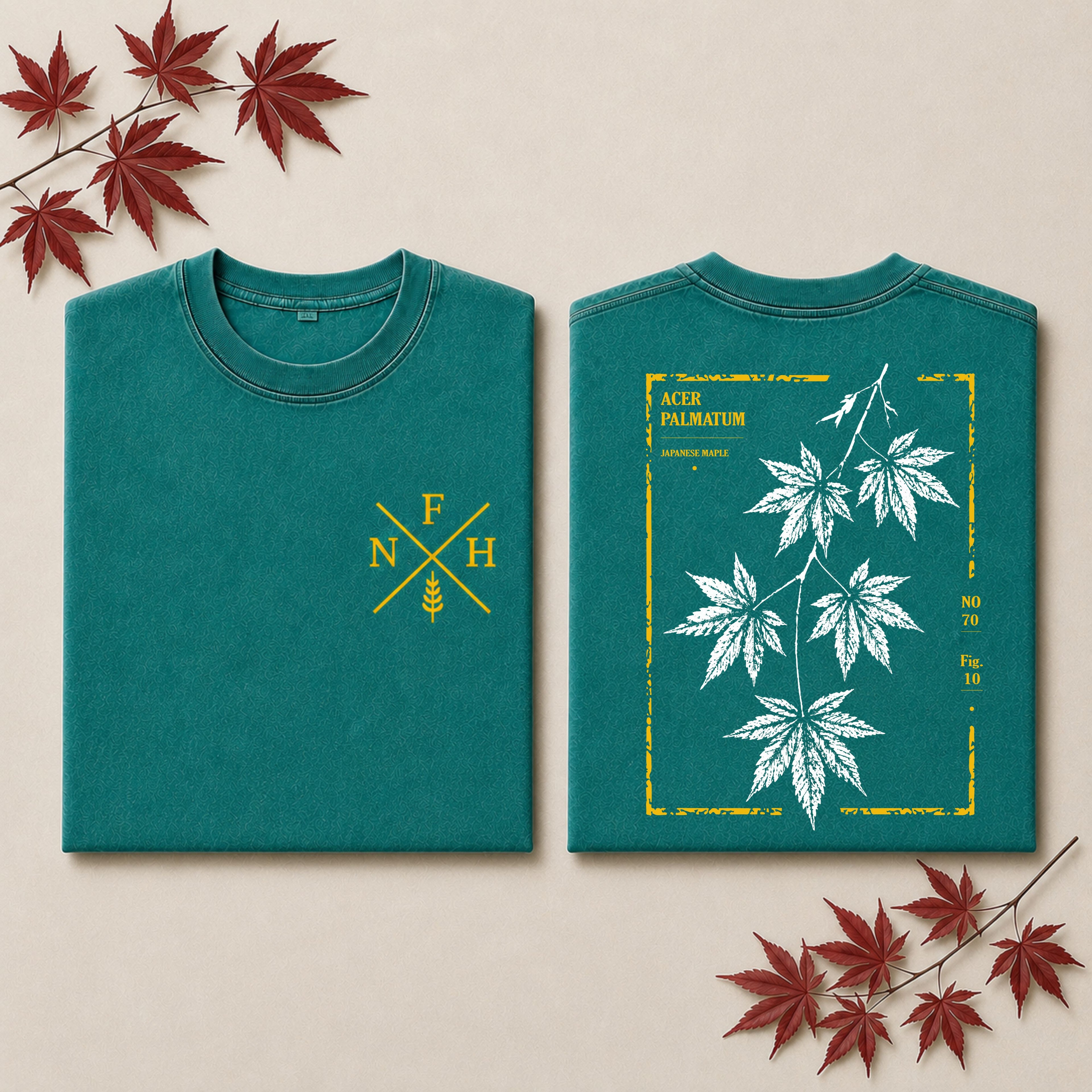 Two folded blue T-shirts displayed side by side on a light stone surface. The left shirt shows a large white fern leaf graphic with gold text and border details, and the right shirt has a small gold monogram logo on the chest.