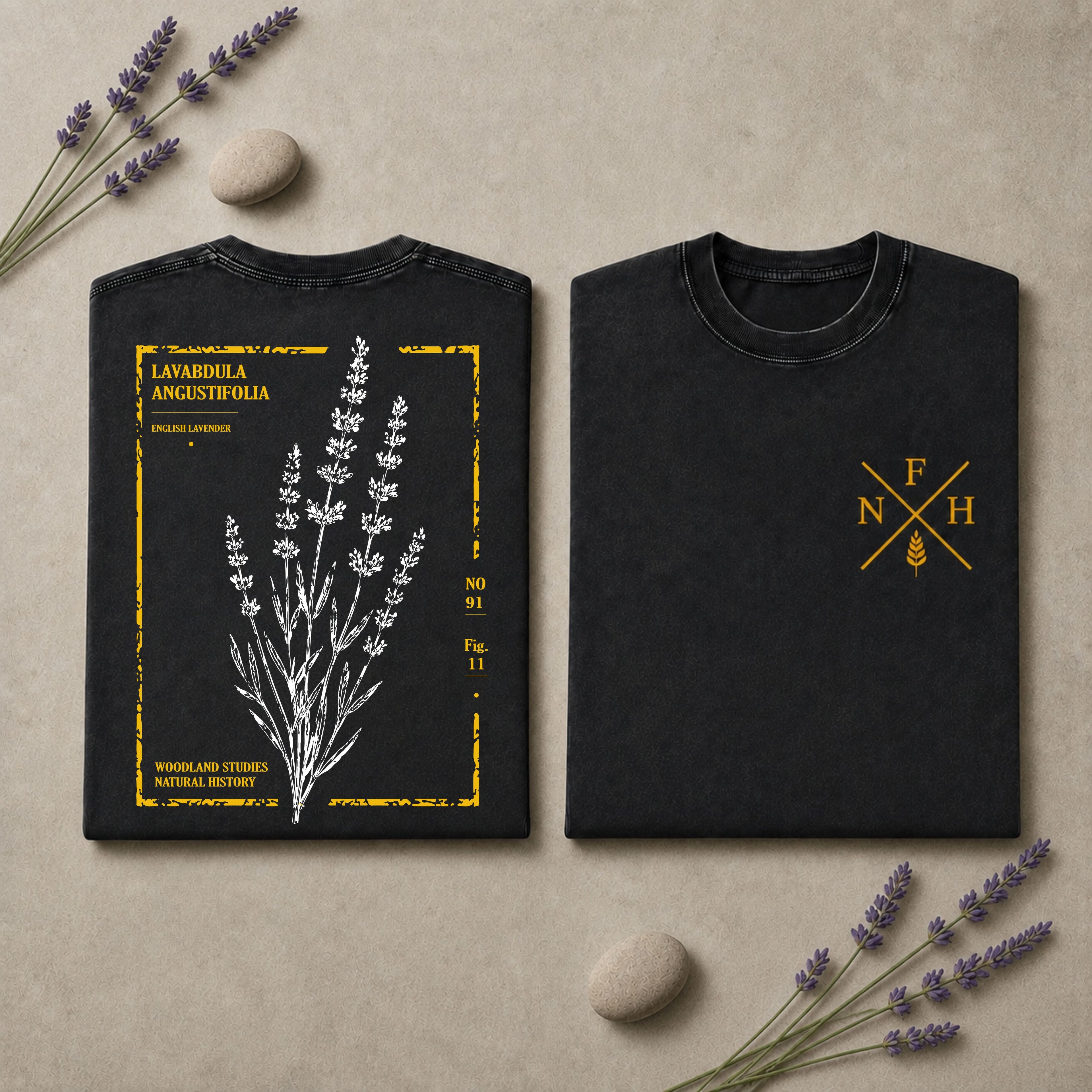 Two black short-sleeve T-shirts laid flat on a beige surface with lavender sprigs and small stones. The left shirt shows a white botanical lavender illustration with yellow text and border details, and the right shirt has a small yellow monogram-style logo on the chest.