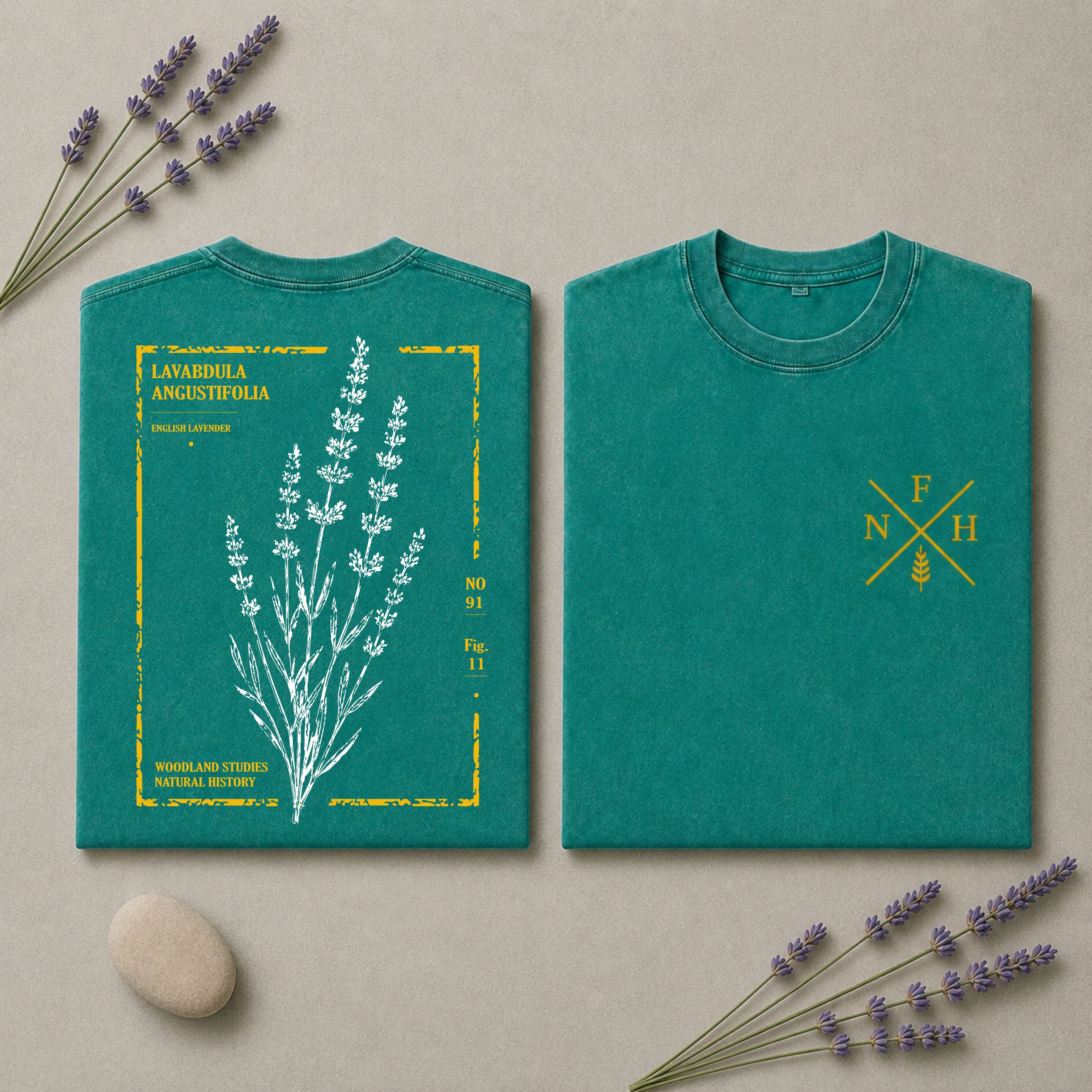 Two views of a teal short-sleeve T-shirt laid flat on a beige surface with lavender sprigs and a stone. The left view shows a large white botanical illustration with yellow text reading 'LAVANDELA ANGUSTIFOLIA' and small yellow details.