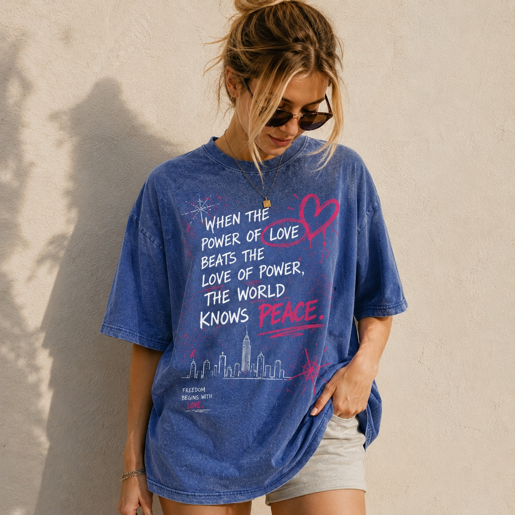 Model wearing a light blue snow washed oversized graphic t-shirt featuring the "When the Power of Love Beats the Love of Power" design, premium heavyweight cotton unisex streetwear tee with a relaxed oversized fit.