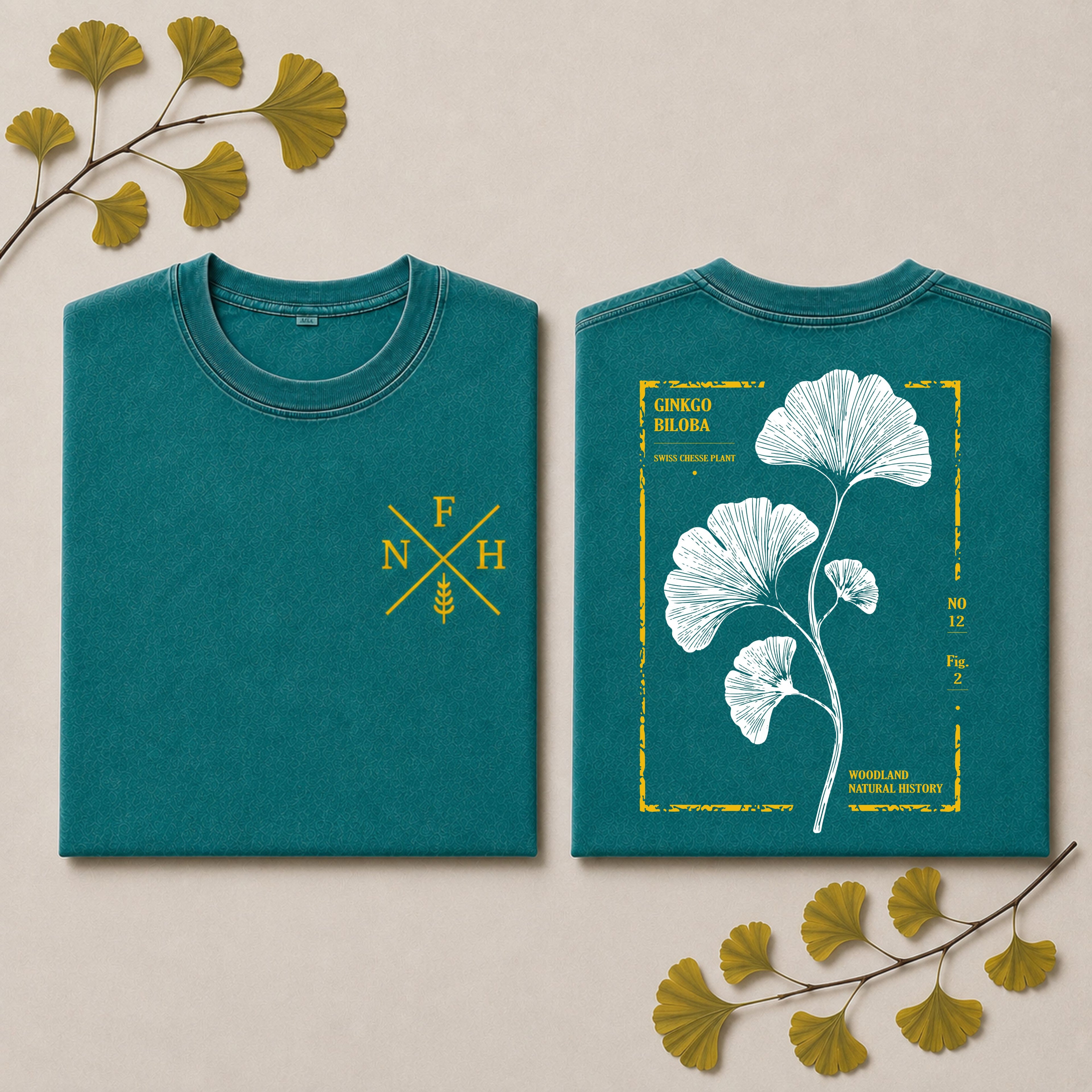 Two folded teal T-shirts shown on a light beige background with decorative ginkgo leaves. The front view has a yellow crossed-FNH monogram with a wheat stalk, and the back view has a large white ginkgo leaf illustration inside a yellow border with text including 'GINKGO BLAURA' and 'CINCO DE MAYO'.