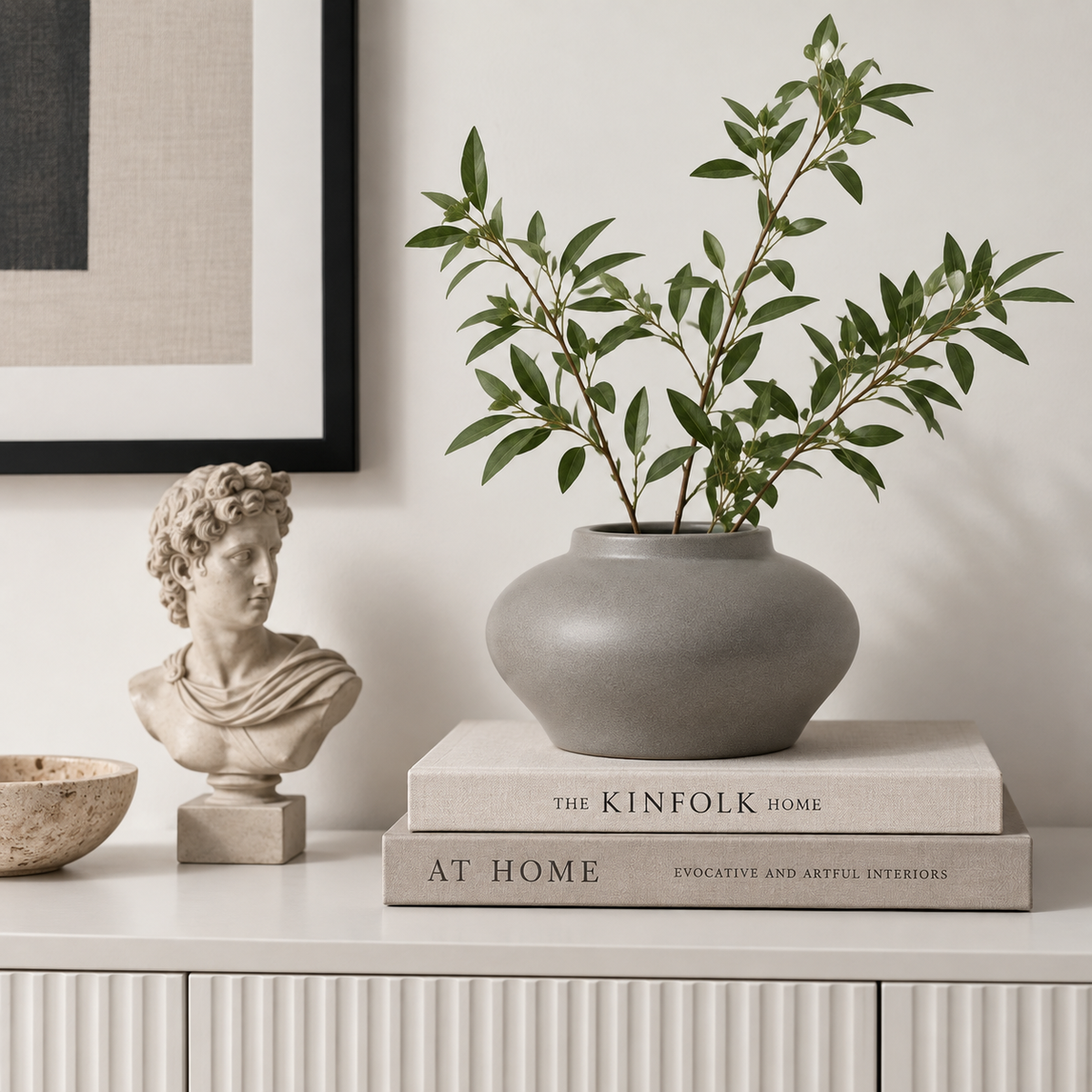 Gray ceramic vase styled with books and sculpture on a light sideboard