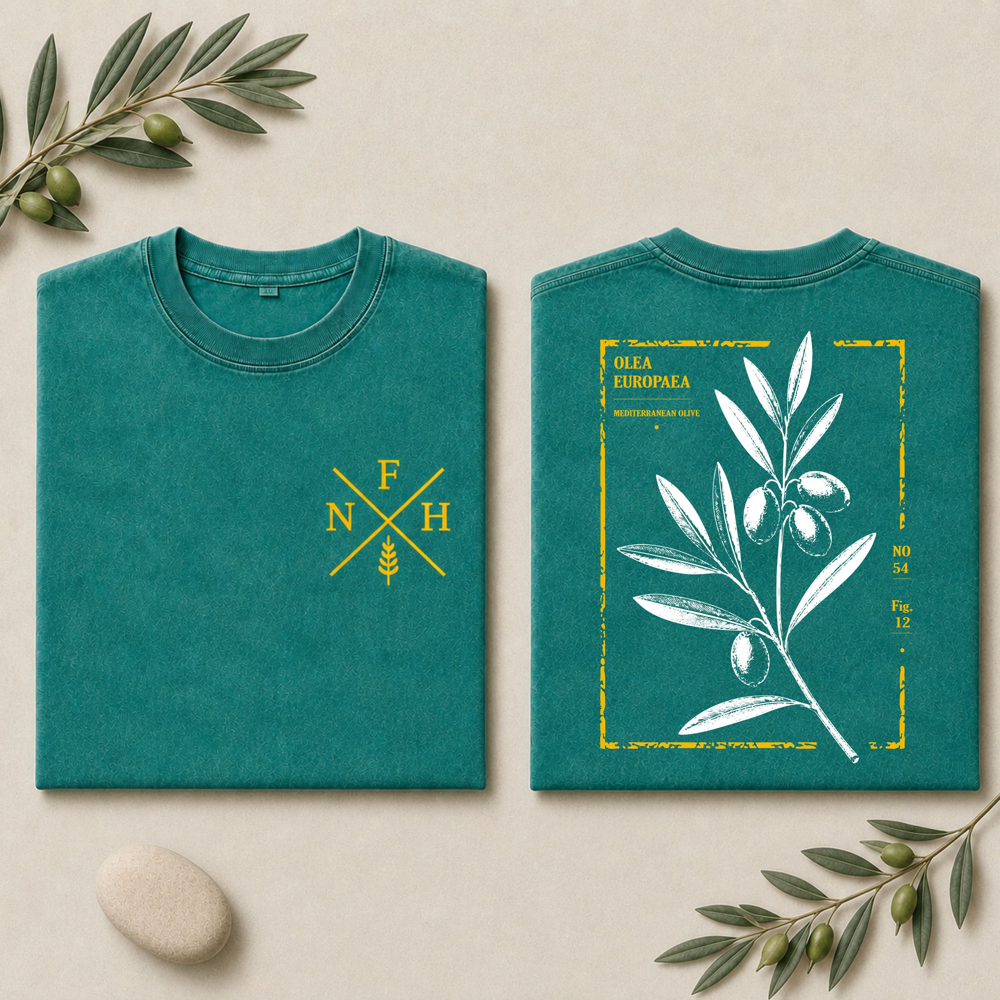 Two folded teal T-shirts shown side by side on a light beige background with olive branches and a stone. The left shirt has a small yellow chest logo with letters and wheat, and the right shirt has a large white olive branch illustration with yellow text and border.
